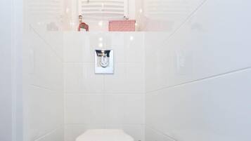 A small, white-tiled bathroom with a toilet, a hand dryer, and a towel rack.