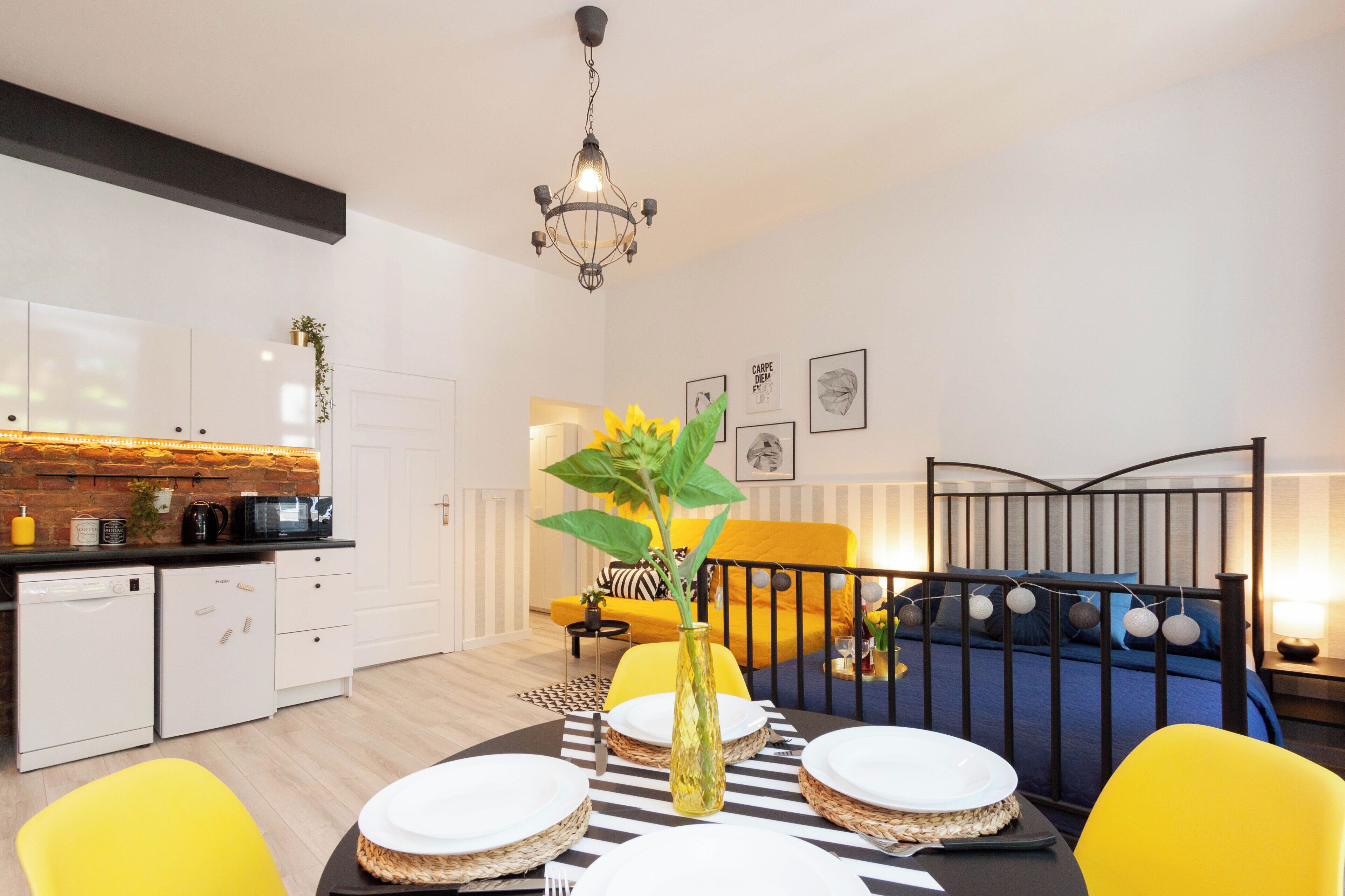 A modern kitchen with white cabinets, a black countertop, and a yellow chair. There is a dining table with plates and a vase with a plant.