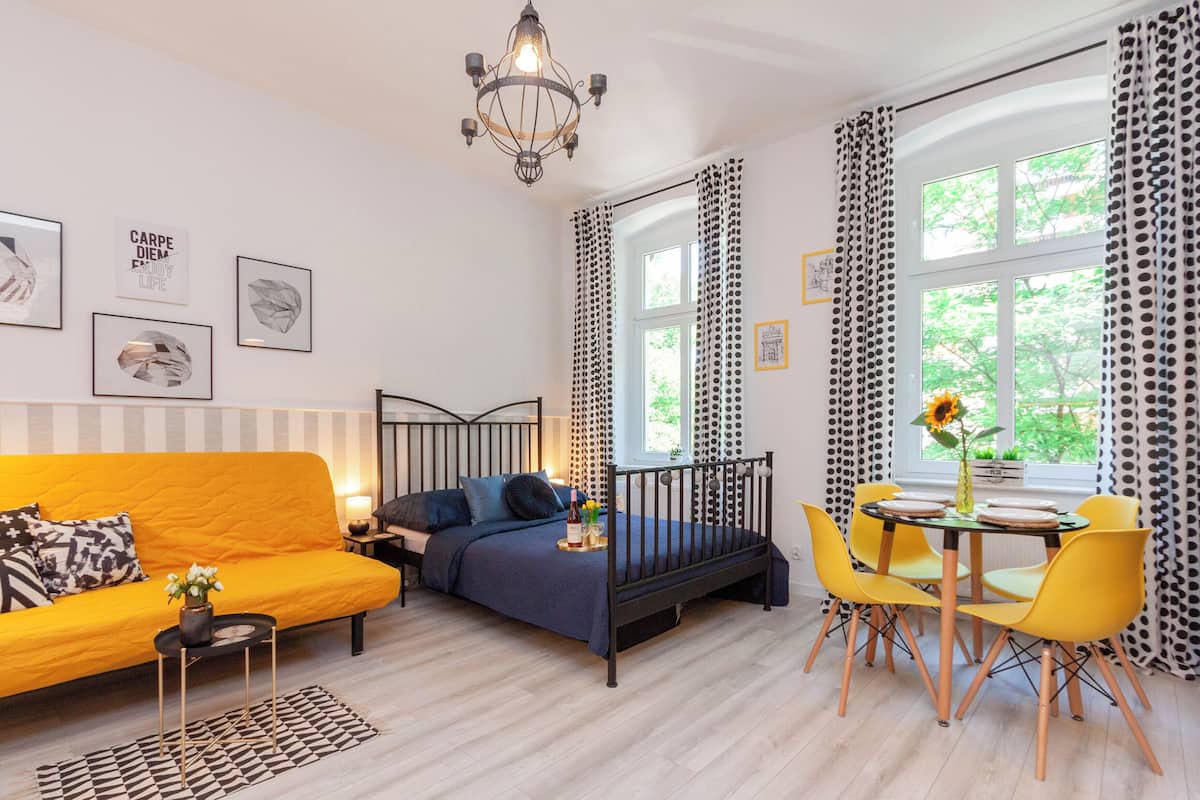 Un espace de vie compact comprenant un lit, un canapé, une table à manger avec des chaises et un lustre.