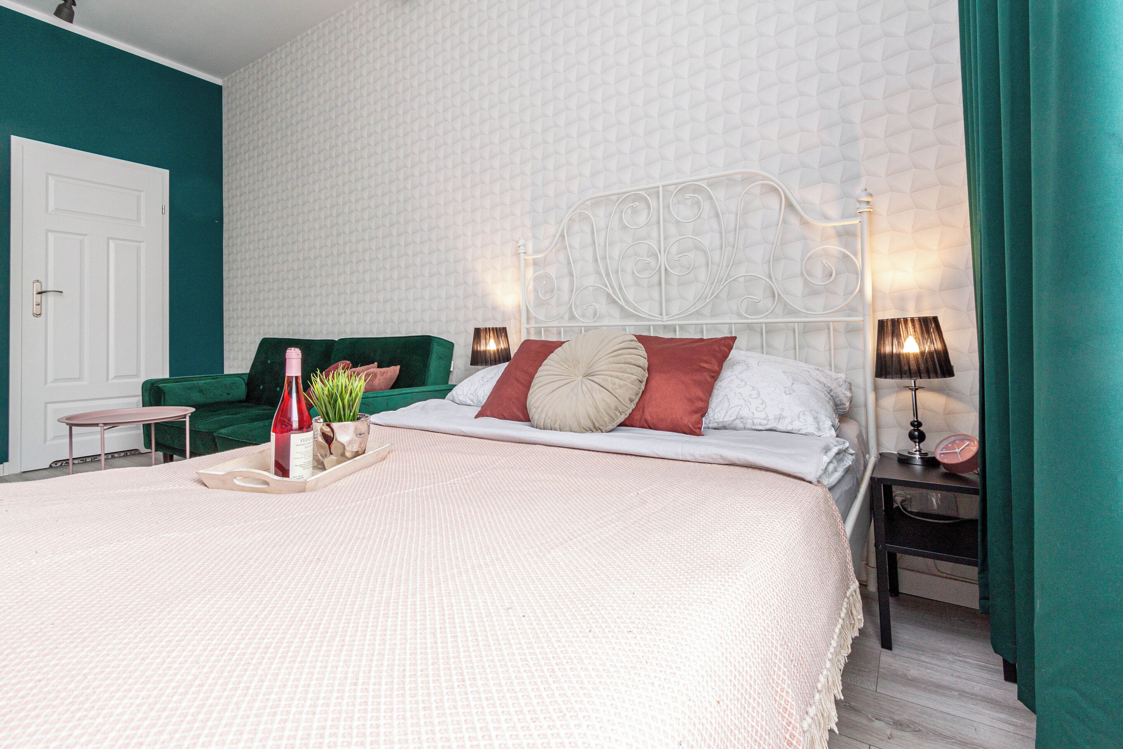 A neatly arranged bedroom with a large bed, a green sofa, a small table, and a bedside lamp.