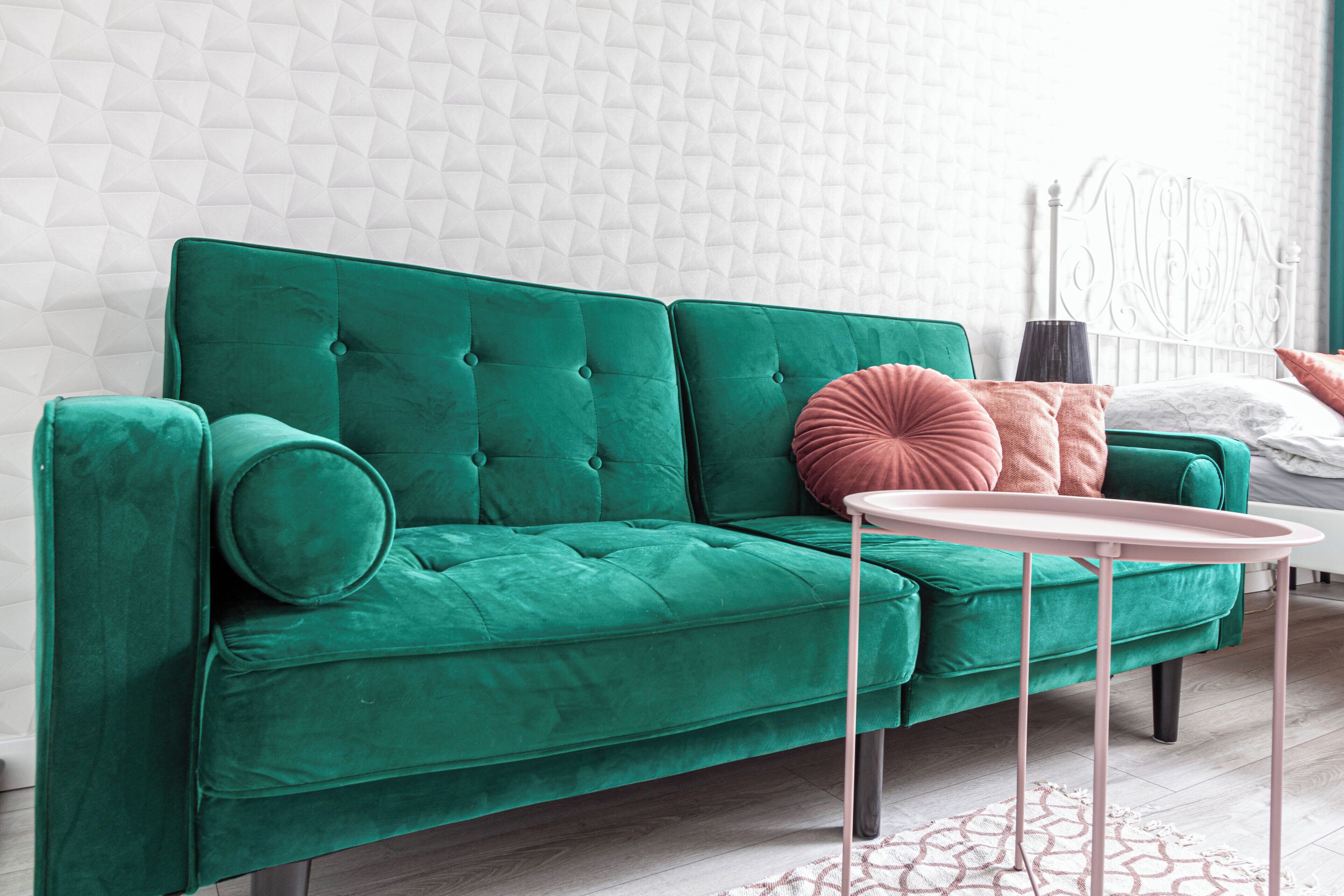 A green sofa with a round table in front, a white headboard, and a patterned wall.