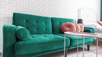 A green sofa with a round table in front, a white headboard, and a patterned wall.