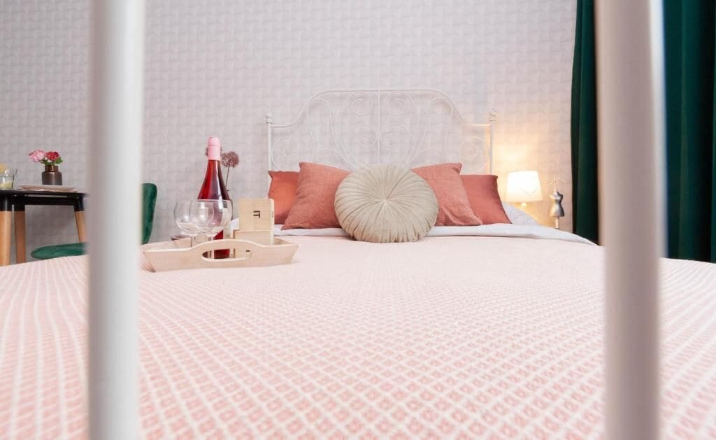 Una cama bien tendida con una colcha estampada, un cojín decorativo y una botella de champán sobre una bandeja.