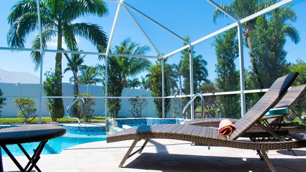 Un espace aménagé au bord de la piscine, avec des chaises longues, une piscine et des palmiers.