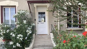 A house with a white door, steps leading to the entrance, and surrounding greenery.