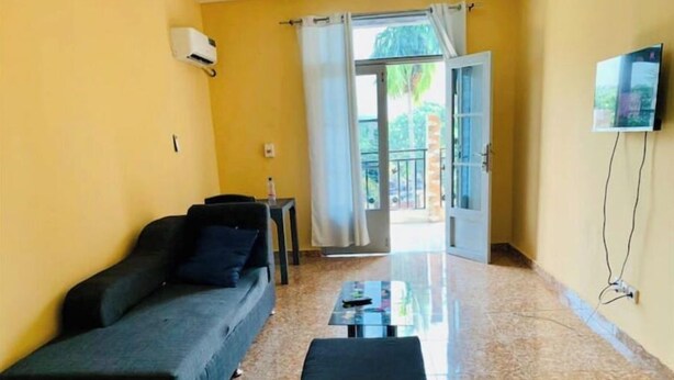 A room with a sofa, a small table, a TV mounted on the wall, and a sliding glass door leading to an outdoor area.