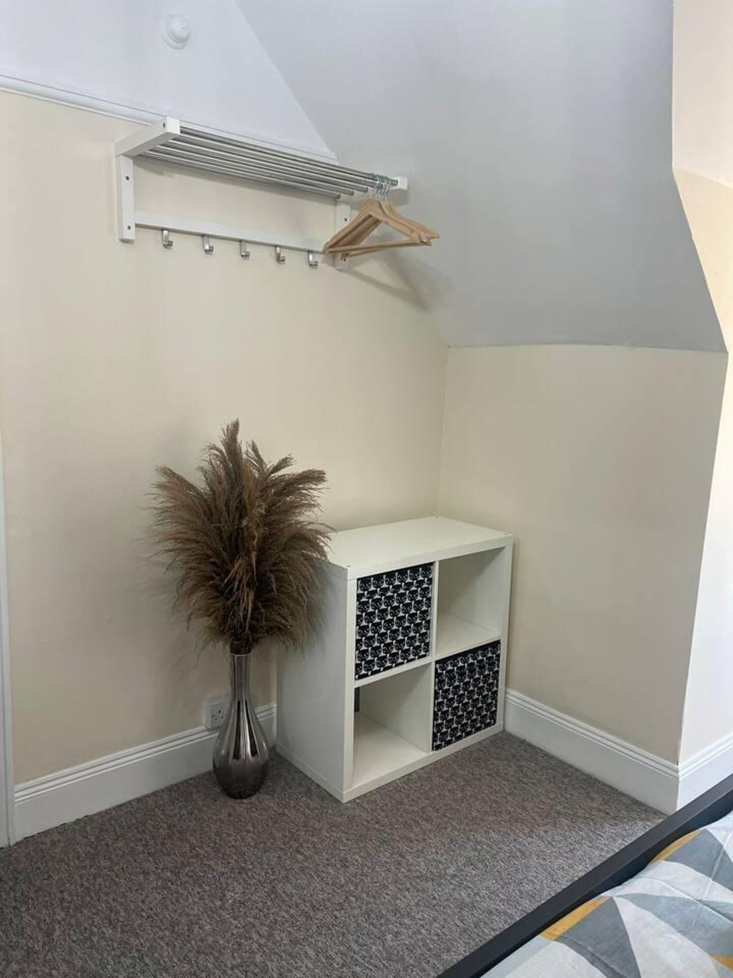 Habitación de esquina con una mesa consola blanca, un perchero y un jarrón alto con plantas secas.