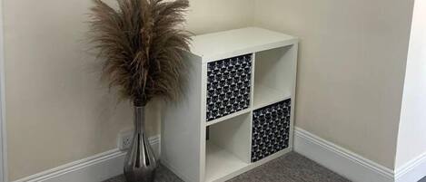 Habitación de esquina con una mesa consola blanca, un perchero y un jarrón alto con plantas secas.