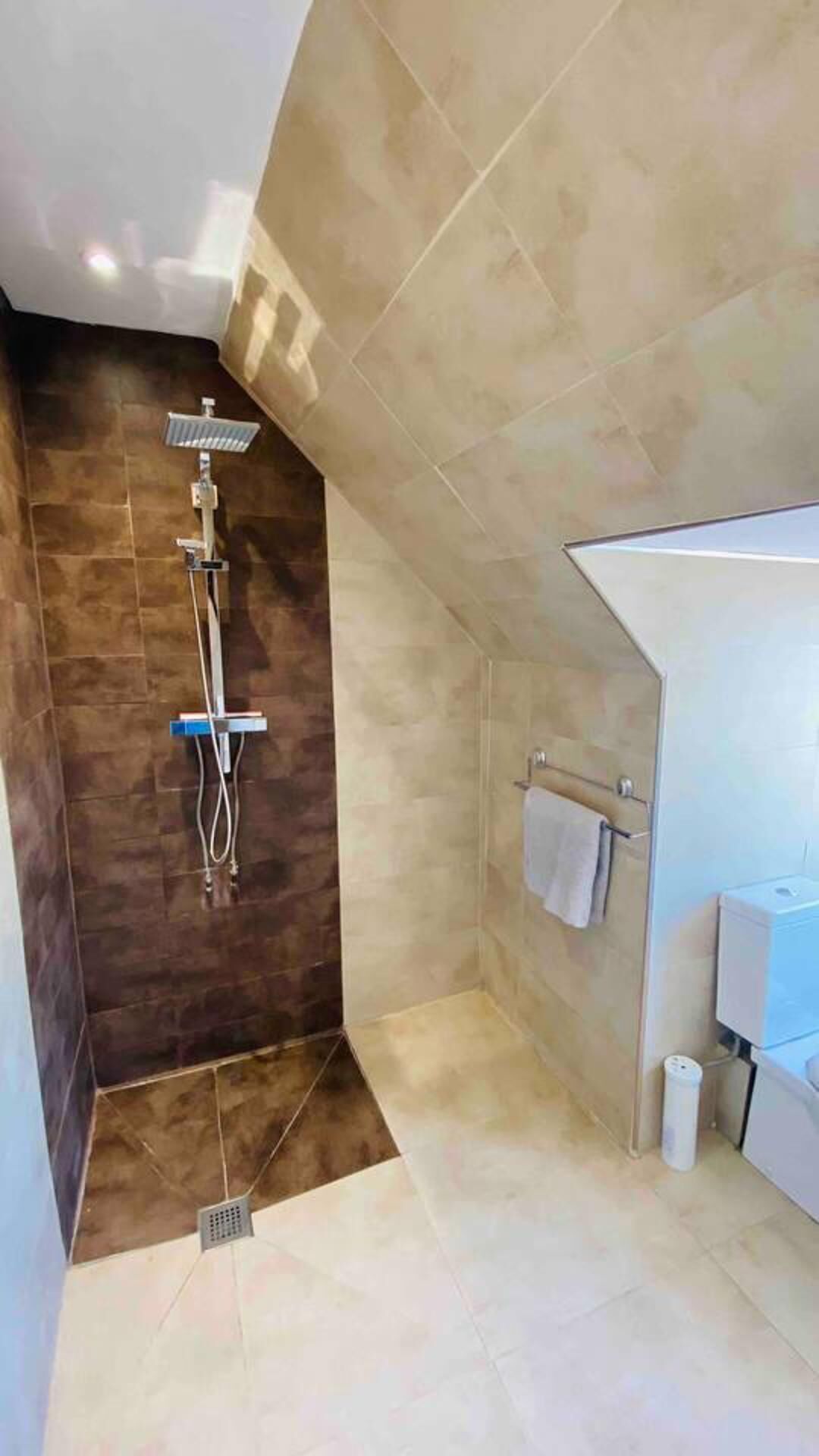 Een moderne badkamer met een douche, toilet en een handdoekhouder.