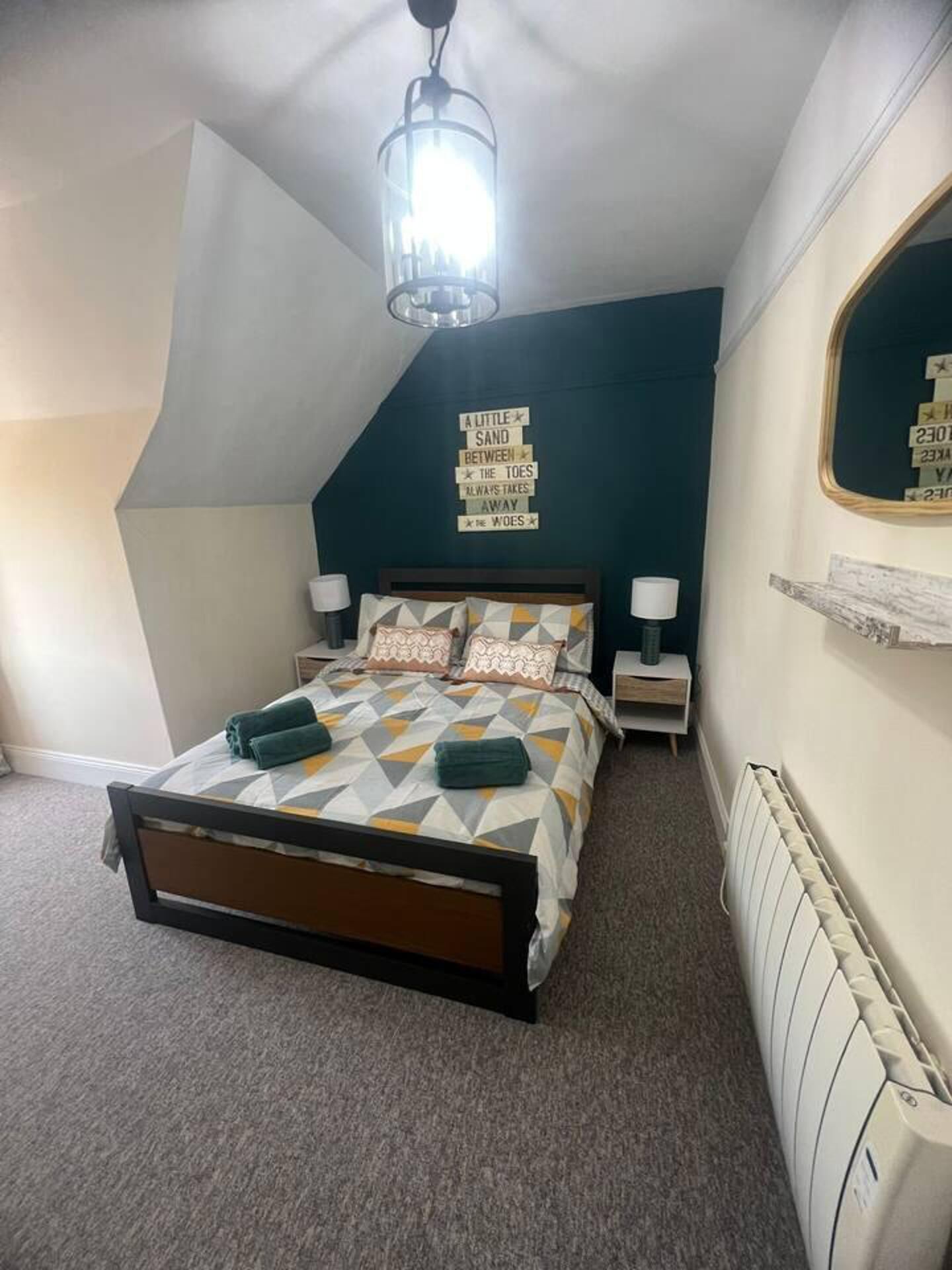 Une chambre à coucher comprenant un lit, des tables de chevet, un miroir et un luminaire au plafond.