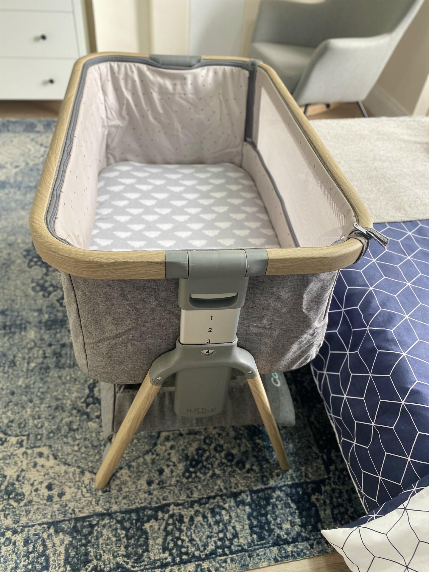 Una cuna de viaje con colchón de estampado gris y blanco, estructura de madera y panel de control gris con botones numerados.