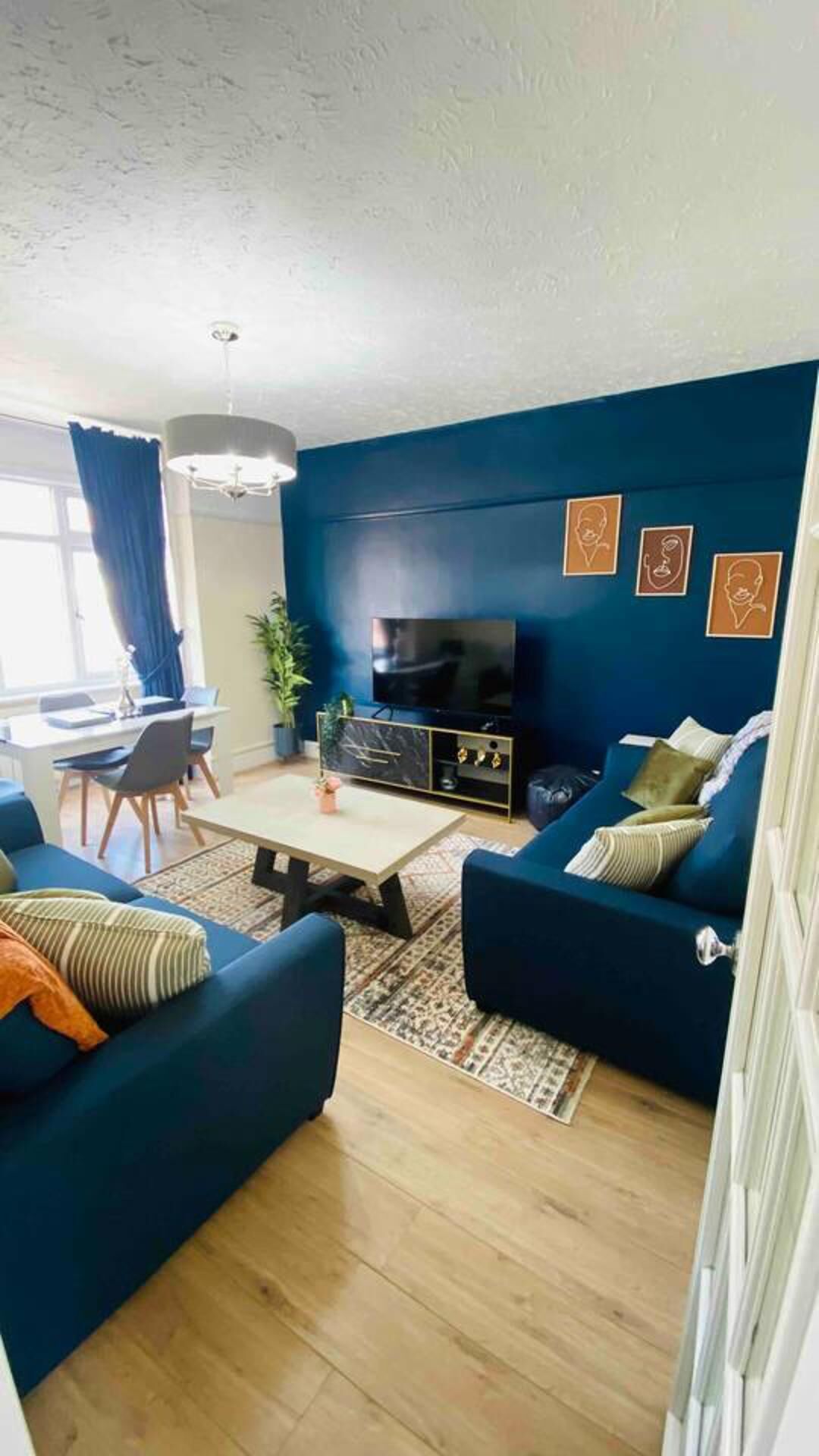 A living room with dark blue walls, a flat-screen TV, a sofa, a coffee table, and a dining area with a table and chairs.