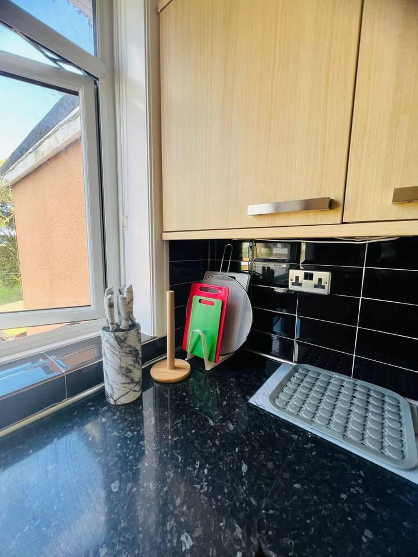 A kitchen with a black countertop, a marble utensil holder, a toaster, and a bread box.