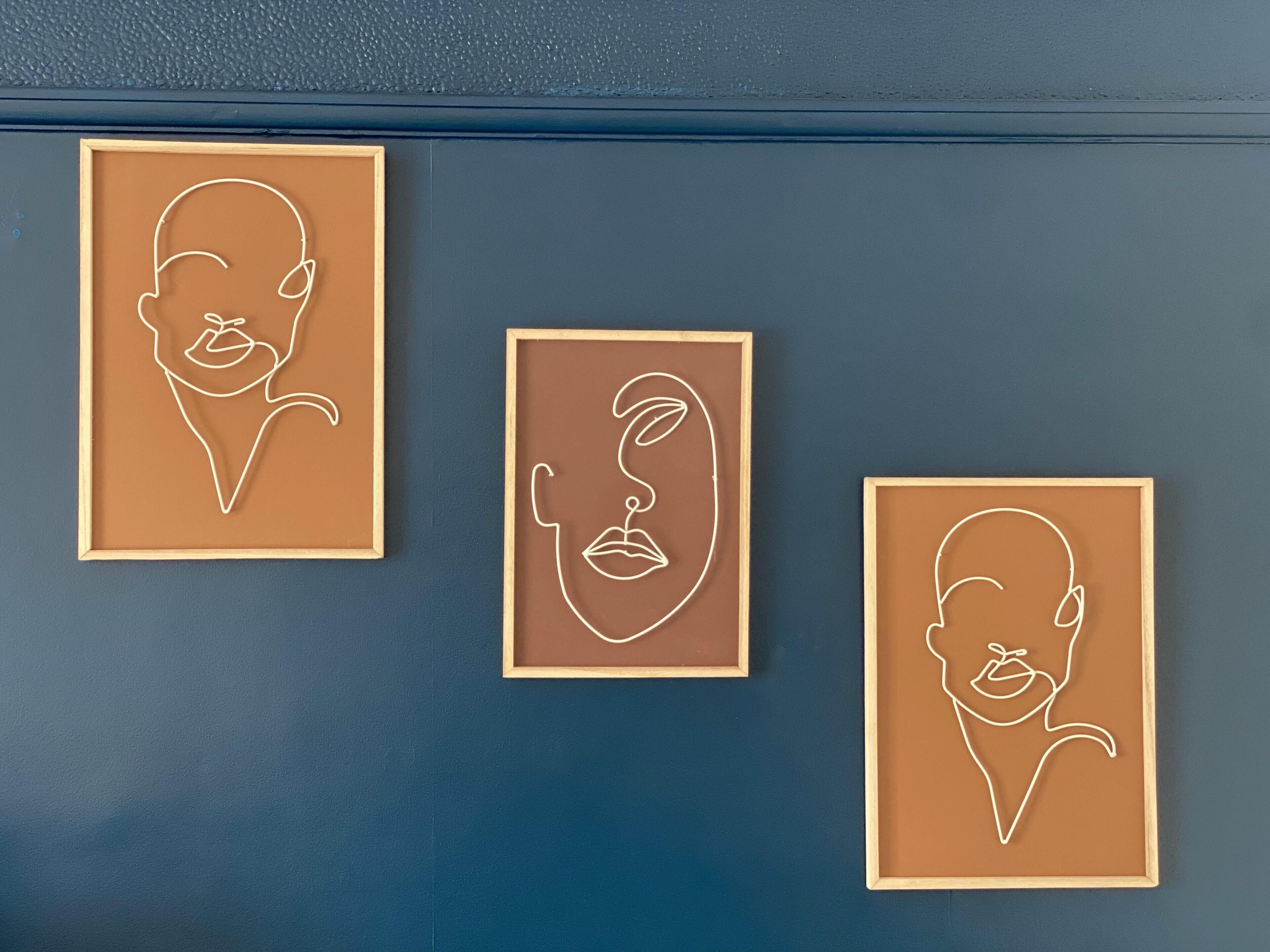 Three framed line drawings of faces on a wall.