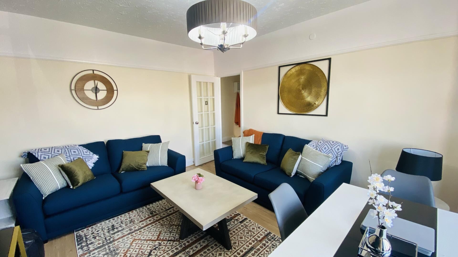 A living room with two blue sofas, a coffee table, a side table with a vase, and a door leading to another room.