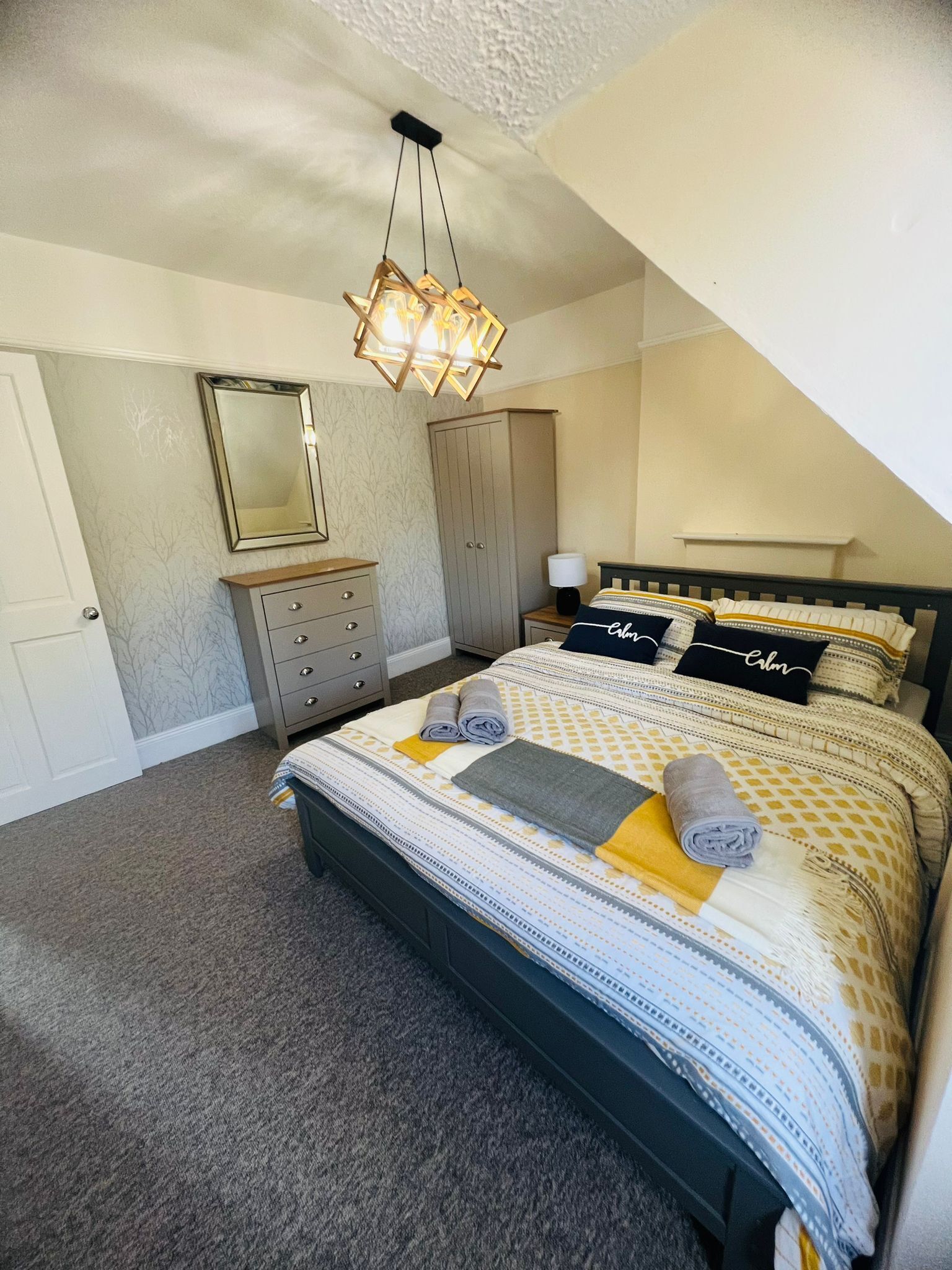 Un dormitorio con cama, cómoda, armario, espejo y lámpara colgante.