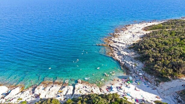 A coastal beach with clear turquoise waters, rocky shoreline, and beachgoers. - Beautiful 4 bedroom villa on peaceful location in village Pavićini (Šegotići)