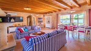 A spacious living area with striped sofas, a dining table with red tablecloth, and a kitchen area with an air conditioning unit. - Beautiful 4 bedroom villa on peaceful location in village Pavićini (Šegotići)