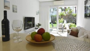 A modern living room with a white sofa, a glass table with a wine bottle and glasses, and a fruit bowl. - Dune Haven in Maspalomas By Pride Holiday Rentals (Playa del Ingles)