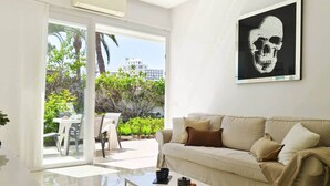 A modern living room with a beige sofa, a coffee table, and a large window overlooking a patio with a table and chairs. - Dune Haven in Maspalomas By Pride Holiday Rentals (Playa del Ingles)
