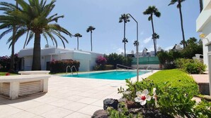 A swimming pool with a tiled deck, surrounded by palm trees and a building with a white facade. - Dune Haven in Maspalomas By Pride Holiday Rentals (Playa del Ingles)