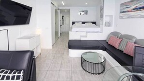 A modern hotel room with a flat-screen TV, a sofa, a bed, a small round table, and a glass coffee table. - Sea View Studio 2 in San Agustin (Maspalomas)