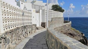 A coastal pathway with stone steps leading to a white building with a patterned fence. - Sea View Studio 2 in San Agustin (Maspalomas)