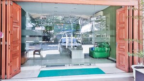 A hotel entrance with a glass door, a green mat, and a car parked outside. - OYO 90381 Belva Guest House (Medan)