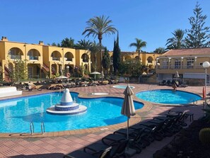 Ein Poolbereich mit zwei Schwimmbecken, einer Zentrobrunnen und Liegestühlen.