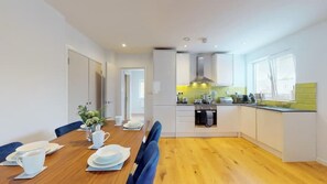 A modern kitchen with white cabinets, a wooden dining table set with plates and cups, and a view of the adjacent dining area.