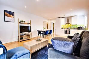 A modern living room with a sofa, coffee table, TV, and dining area.
