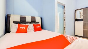 Une chambre d’hôtel avec un lit, deux oreillers rouges ornés du mot « OYO », un couvre-lit blanc et une armoire avec un miroir.