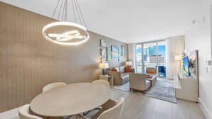 A modern hotel room with a dining area, a sofa set, a TV, and a city view through the window. - ★★★★★ Fascinating 1BD/1BA Beachfront Condo by the Ocean (Hollywood)