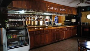 A coffee shop with a wooden counter, shelves of beverages, and a glass display case. - Cabo Tortuga Hotel Boutique (Cabo San Lucas)