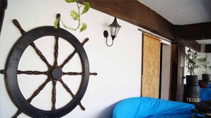 A room with a large wooden ship's wheel on the wall, a blue sofa, and a wooden door. - Cabo Tortuga Hotel Boutique (Cabo San Lucas)