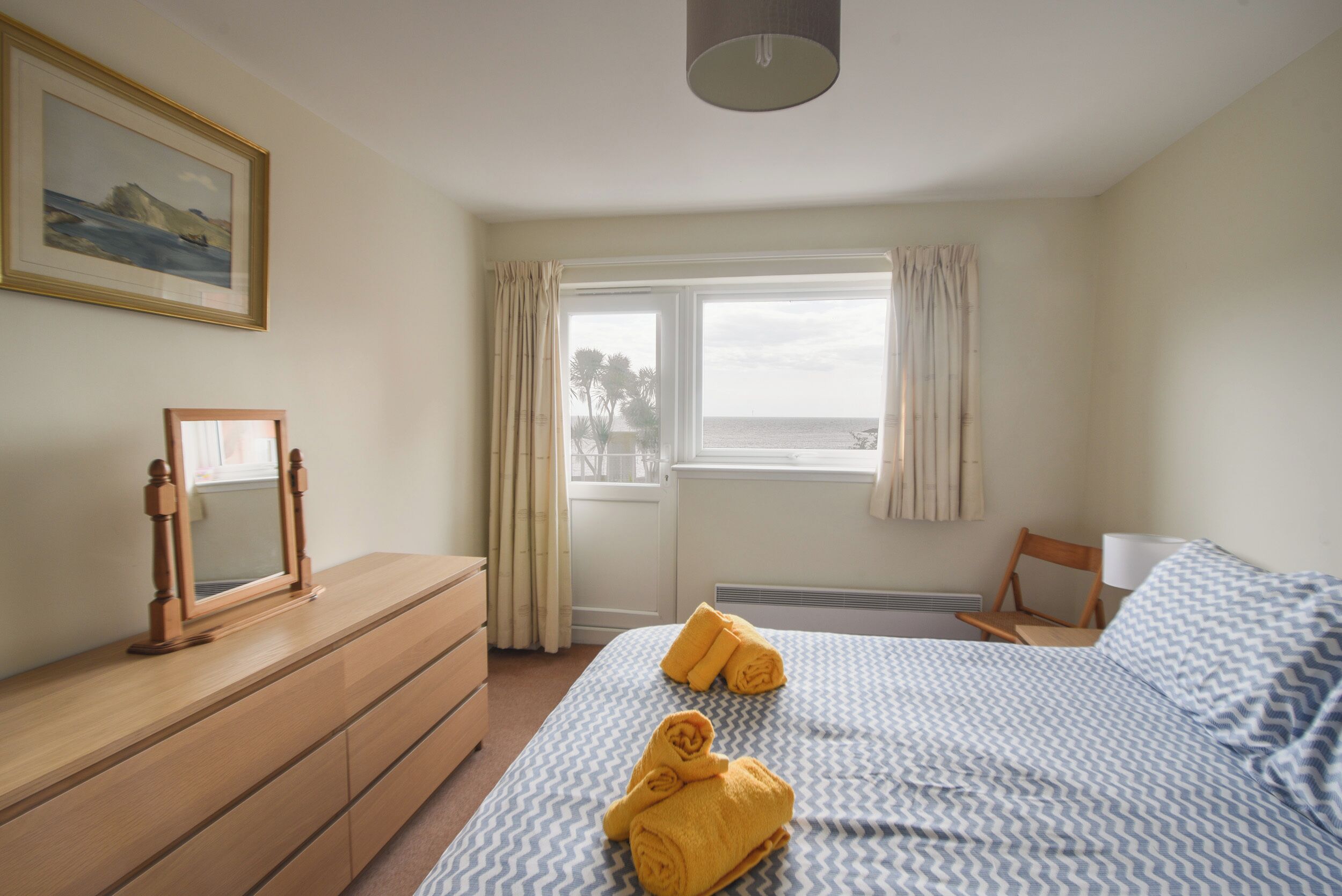 A hotel room with a bed, a dresser, a mirror, and a window with curtains.