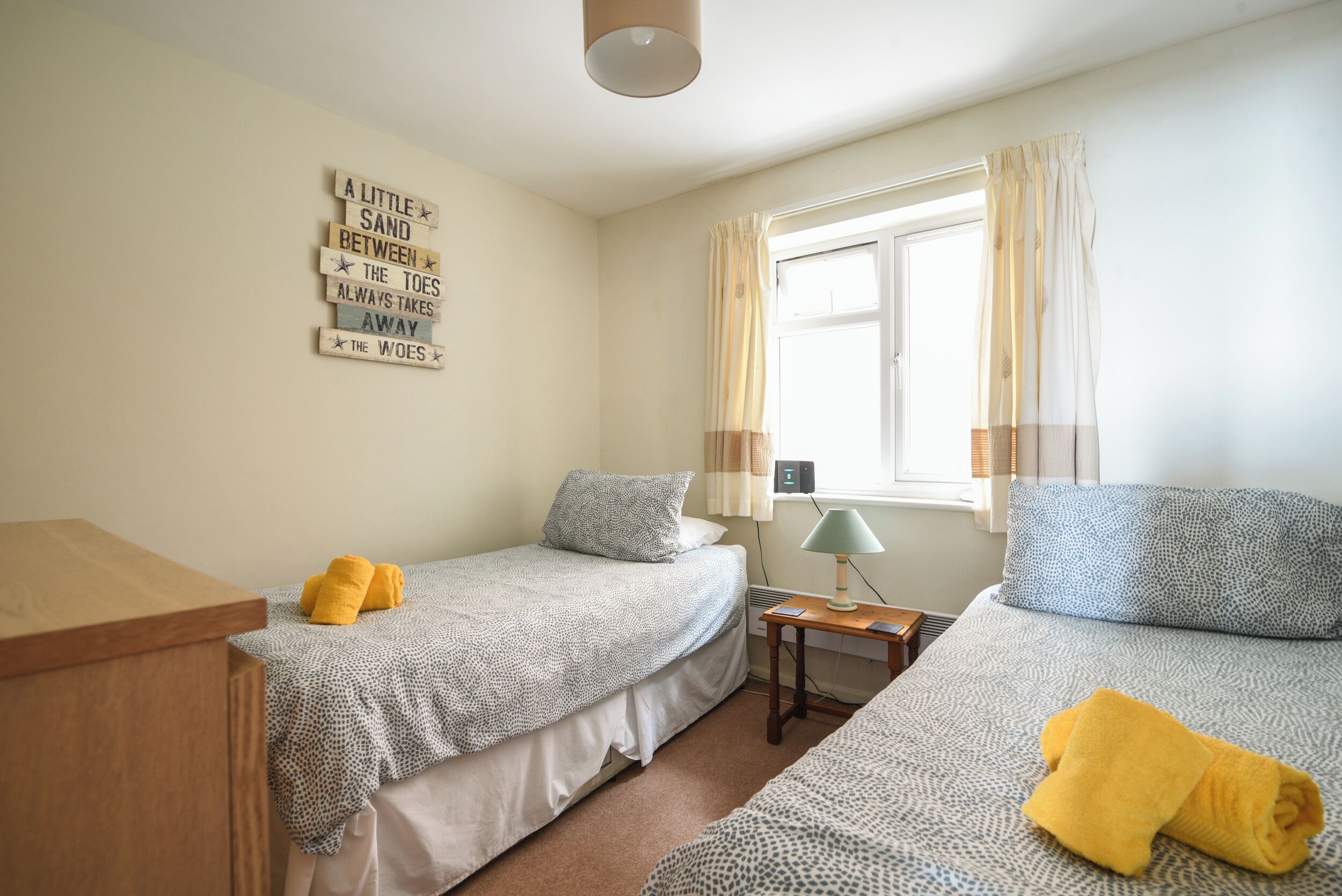 Een kamer met twee bedden, een houten bureau, een lamp en een raam met gordijnen.