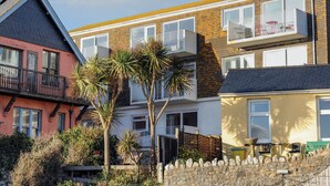 A multi-story residential building with balconies, a stone wall, and a small garden area with palm trees. - 3 Bay View Court (Lyme Regis)