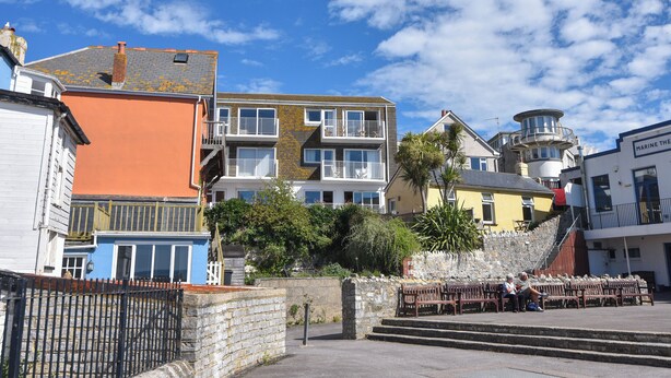 A coastal building with multiple balconies, a stone wall, and a clear blue sky. - 3 Bay View Court (Lyme Regis)