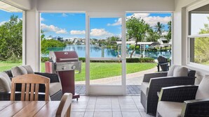 A patio with a grill, outdoor seating, and a view of a swimming pool and buildings. - Serene Bayfront Stay - Dock, Hot Tub, Close to Beach (Bonita Springs)