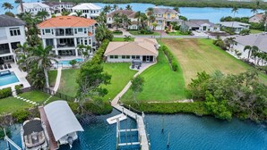 A residential area with a dock, a swimming pool, and a large house with a red roof. - Serene Bayfront Stay - Dock, Hot Tub, Close to Beach (Bonita Springs)