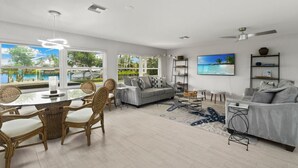 A spacious living room with a dining area, large windows, a pool view, and a ceiling fan. - Serene Bayfront Stay - Dock, Hot Tub, Close to Beach (Bonita Springs)