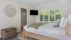 Une chambre à coucher comprenant un lit, une télévision, une fenêtre avec des stores, un miroir et un panier en osier.