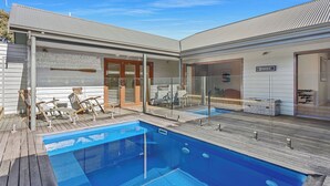 Une maison moderne dotée d’une piscine, d’une terrasse en bois et de chaises longues.