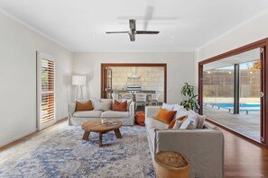 A spacious living area with a ceiling fan, a dining area with a kitchen, and a view of a pool through large sliding doors.