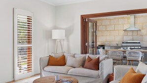 Un salon avec un canapé, des fauteuils, une table basse et une cuisine visible à travers une porte ouverte.