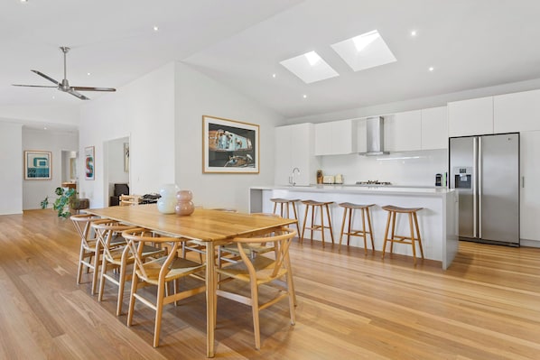 A modern kitchen with white cabinets, a stainless steel refrigerator, and a wooden dining table with chairs.