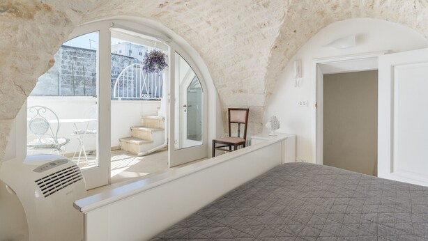 Une chambre avec un plafond en pente, une grande fenêtre, un lit, une chaise et un radiateur.