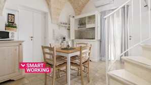 Une cuisine avec des meubles blancs, une table à manger avec des chaises et un escalier.