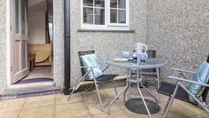 A patio area with a table and chairs, a window, and a door leading to an interior space. - Ty Bach Twt (Conwy)